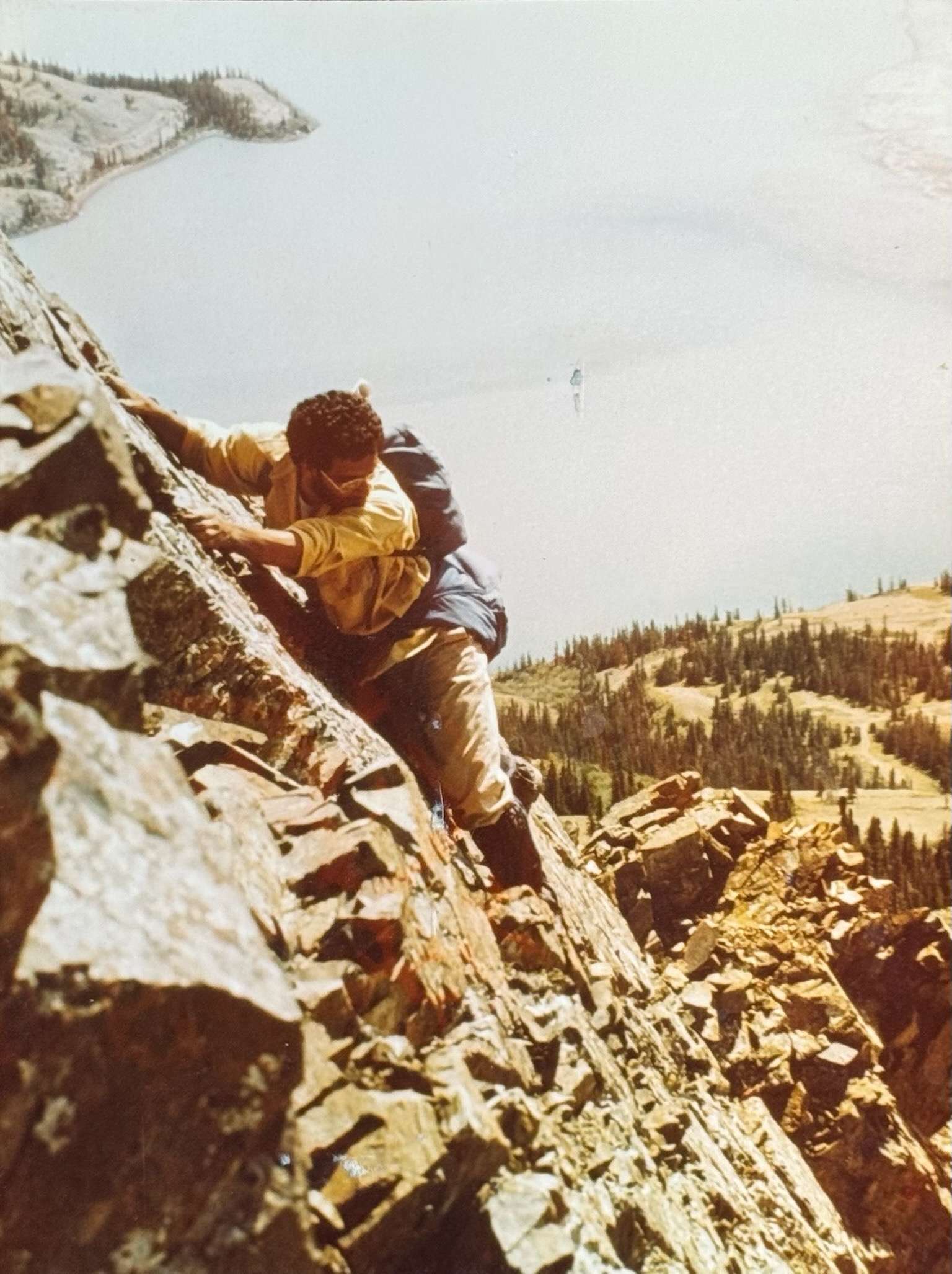 Kluane National Park and Reserve YukonCanada ‣ I Have An Idea Two climbers ascend a steep rocky mountainside with a valley and forest below; one climber leads the way while gripping the rock.