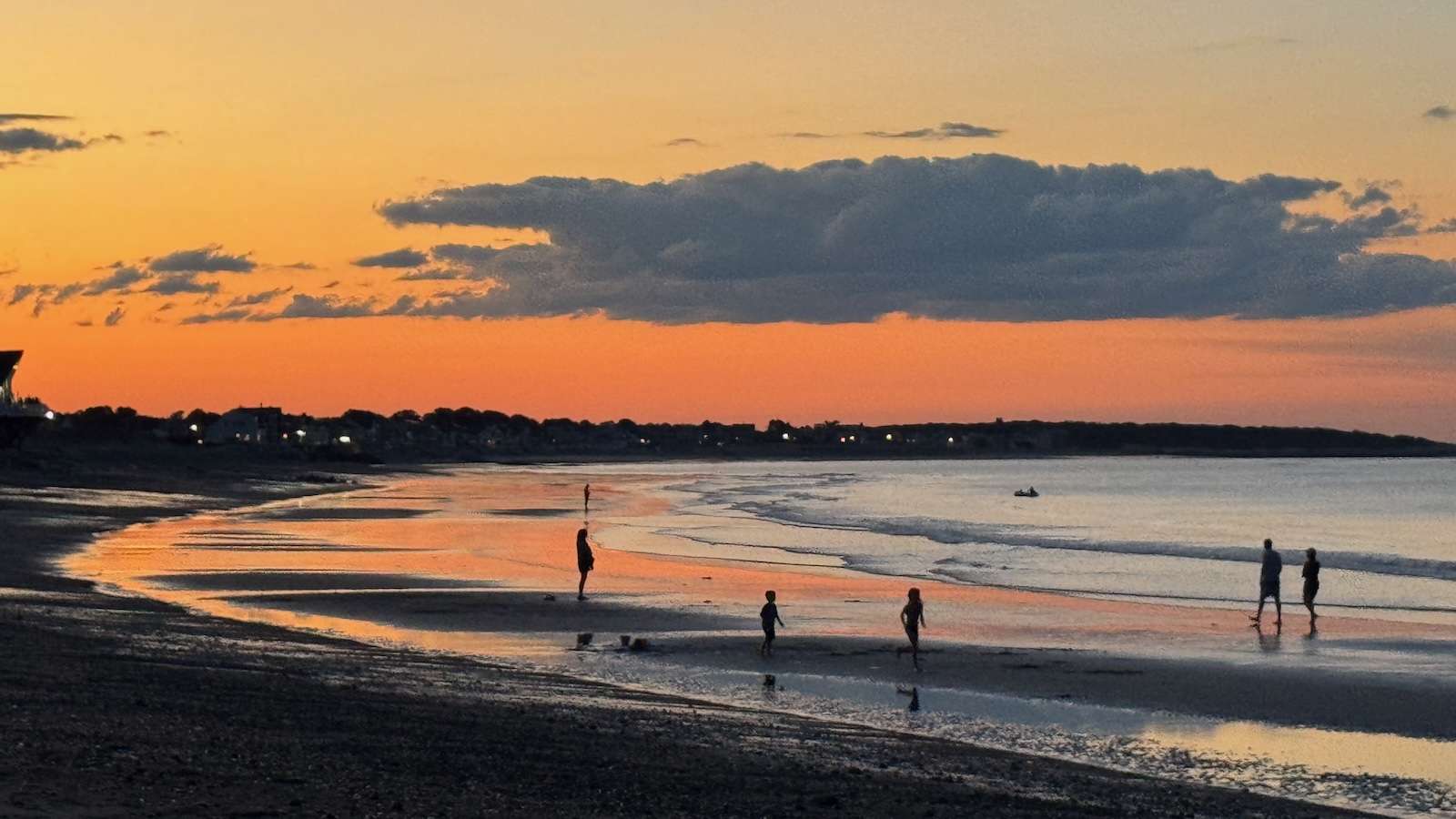 IMG_1994 ‣ I Have An Idea Sunset beach with orange sky, calm water, and silhouetted people walking along the shoreline.